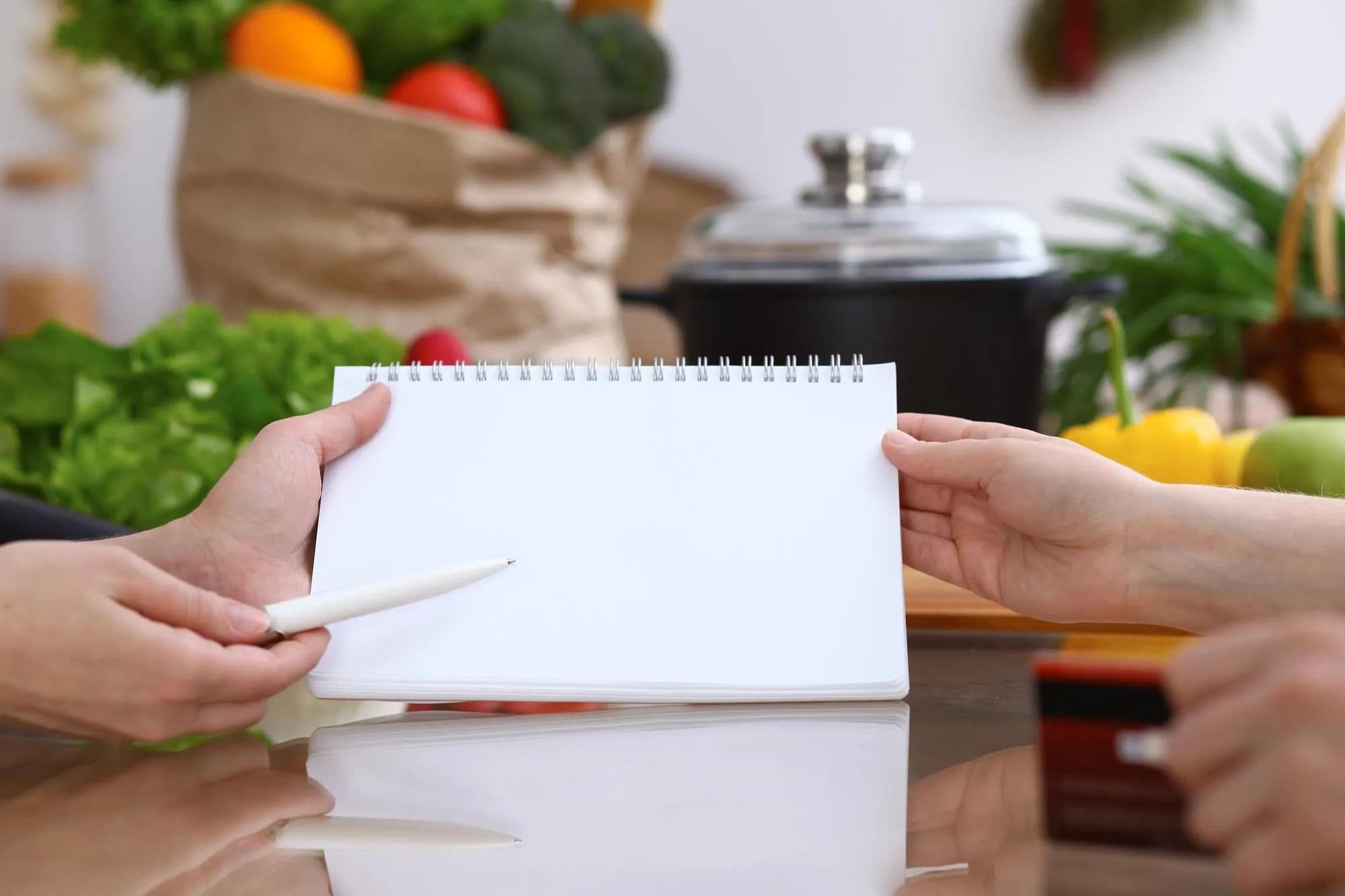 Duas pessoas começam juntas um planejamento semanal de refeições em um caderno vazio